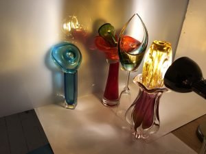 An arrangement of differently coloured glass objects with a light shining though onto a sheet of perspex.